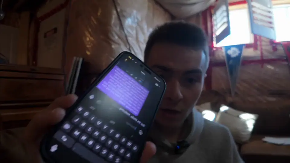 Aidan Holt holding his phone up to the camera; the screen shows a dictated message in a chat app above the keyboard. The text is not readable.